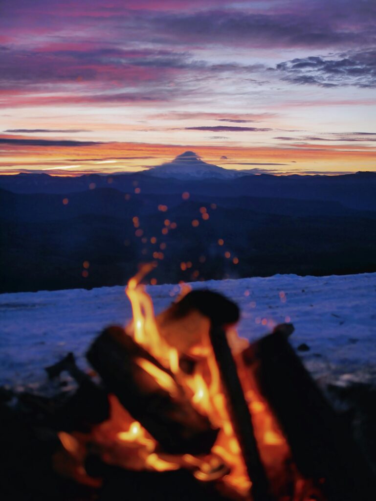 pexels-photo-3551234-3551234 A warm campfire overlooking a majestic mountain silhouette against a colorful sunset sky.